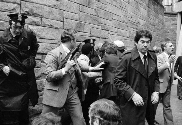 In this March 30, 1981 file photo, Secret Service agents and police officers swarm a gunman, obscured from view, after he attempted an assassination on President Ronald Reagan outside the Washington Hilton hotel. (AP Photo/Ron Edmonds, File)