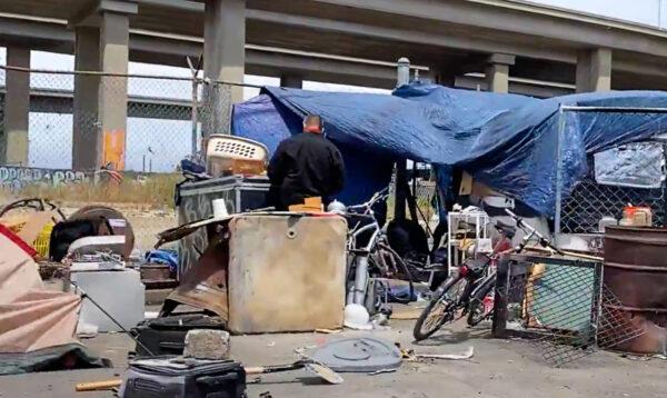 A person stands in front of an encampment under I-880 in Oakland, Calif., on May 26, 2022. (Cynthia Cai/NTD Television)
