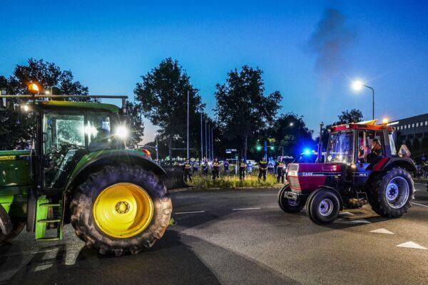 Tractors drive by Dutch police officers standing guard as police close access to Apeldoorn on the A1 highway to block farmers from demonstrating against the Dutch government's plans to cut nitrogen emissions, on June 29, 2022. (JEROEN JUMELET/ANP/AFP via Getty Images)