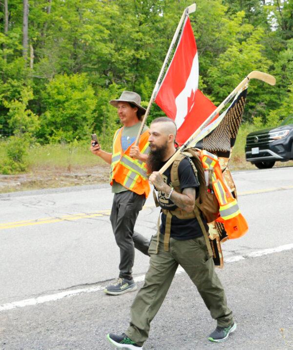 Dan Jones (L), part of James Topp's team, walks with the Canadian flag on a rural road west of Ottawa on June 29, 2022. (Noé Chartier/The Epoch Times)