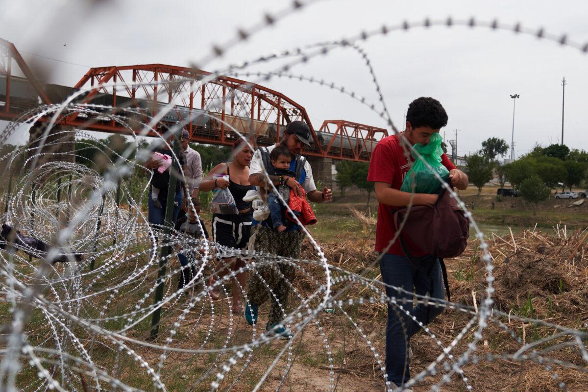 Illegal immigrants who crossed the Rio Grande walk along concertina wire in Eagle Pass, Texas, on May 22, 2022. (Allison Dinner/AFP via Getty Images)