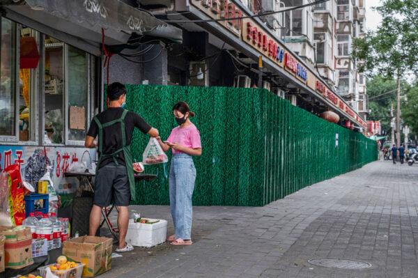 A woman buys food from a shop next to a fenced-off business area and residential compound that has been locked down due to a COVID-19 outbreak on June 16, 2022, in Beijing, China. (Kevin Frayer/Getty Images)