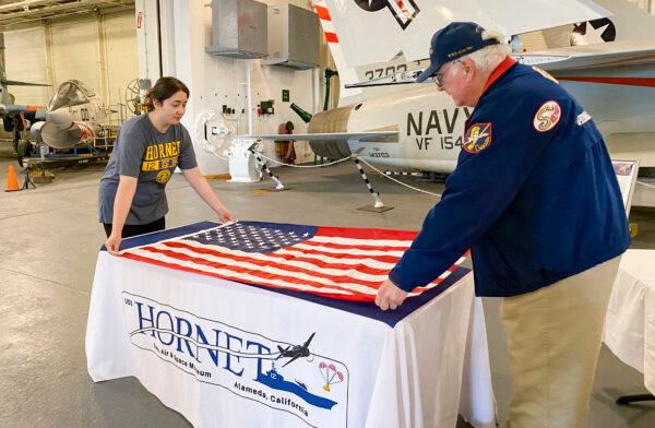 Keila Hurtado and Richard Keefer prepare to fold a U.S. flag at the USS Hornet Museum in Alameda, Calif., on June 28, 2022. (Ilene Eng/NTD Television)