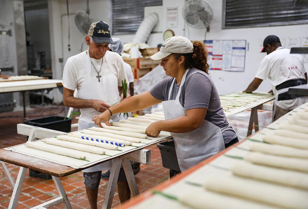 Yovanni Perdomo (36), middle, and Carlos Cabota (56), left, of Tampa place palmetto leaves on loaves and flip them at La Segunda Central Bakery in Ybor City. (Lauren Witte/Tampa Bay Times/TNS)