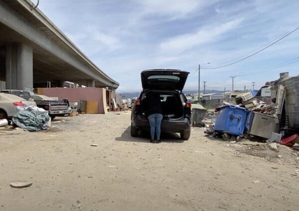 An unidentified person stands with a car parked in a homeless encampment under I-880 in Oakland, Calif., on May 26, 2022. (Cynthia Cai/NTD Television)