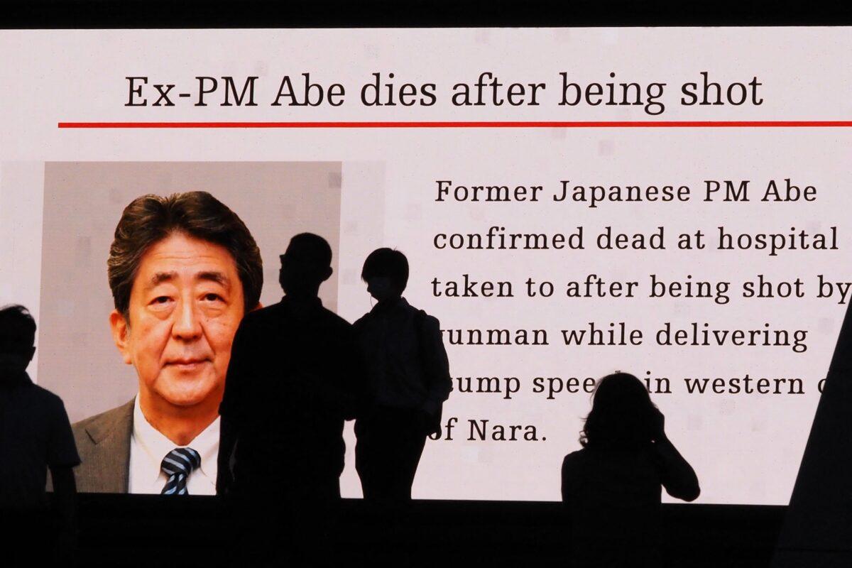 Pedestrians are silhouetted against a large public video screen showing an image of former Japanese prime minister Shinzo Abe in the Akihabara district of Tokyo on July 8, 2022, after he was shot and killed in the city of Nara. (Toshifumi Kitamura/AFP via Getty Images)