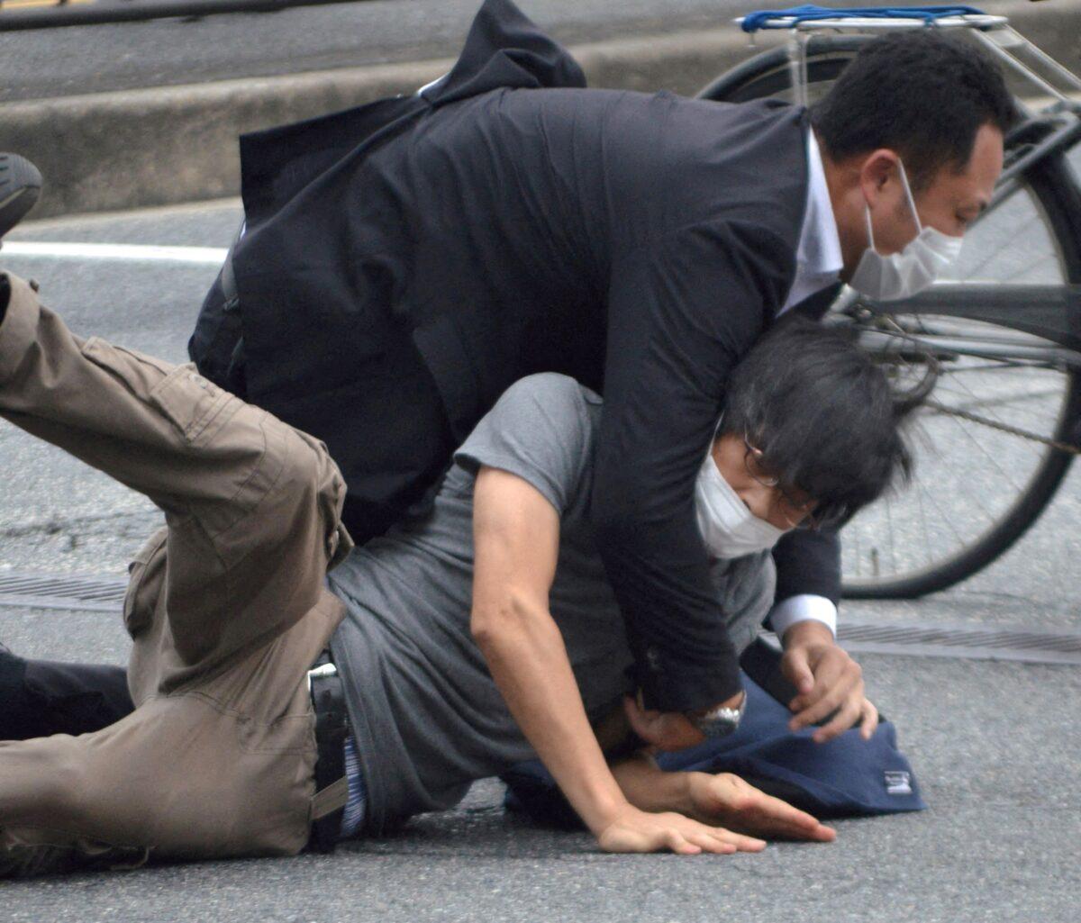 A man, believed to be a suspect in shooting former Japanese Prime Minister Shinzo Abe, is held by police officers at Yamato Saidaiji Station in Nara, Nara prefecture, on July 8, 2022. (The Yomiuri Shimbun via Reuters)