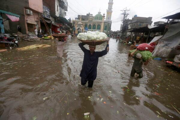Laborers carry produce as they wade through a flooded road after heavy rainfall, in Lahore, Pakistan, on July 21, 2022. (AP Photo/K.M. Chaudary)