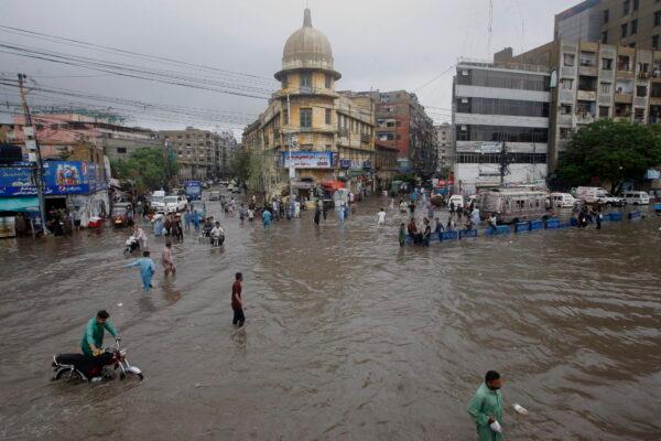 Motorcyclists and people wade through a flooded road in a business district after a heavy rainfall in Karachi, Pakistan, on July 9, 2022. (Fareed Khan/AP Photo)