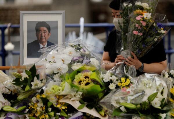 A mourner offers flowers next to a picture of late former Japanese Prime Minister Shinzo Abe, who was shot while campaigning for a parliamentary election, on the day to mark a week after his assassination at the Liberal Democratic Party headquarters in Tokyo, Japan, on July 15, 2022. (Issei Kato/Reuters)