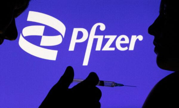 People pose with syringe in front of the displayed Pfizer logo in this photo, taken on December 11, 2021. (REUTERS/Dado Ruvic/Illustration/File Photo)