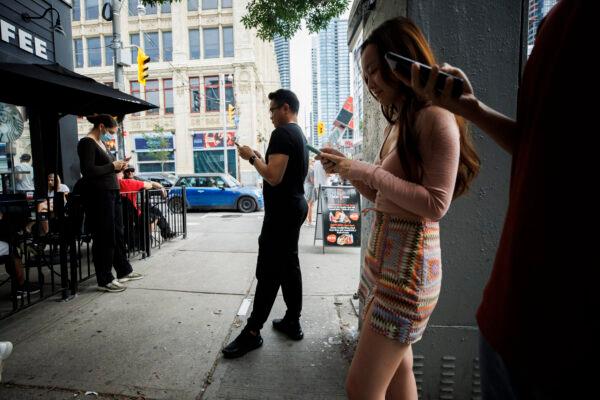 People use electronics outside a coffee shop in Toronto on July 8, 2022 amid a nationwide Rogers outage that affected many of the telecommunication company's services. (The Canadian Press/Cole Burston)