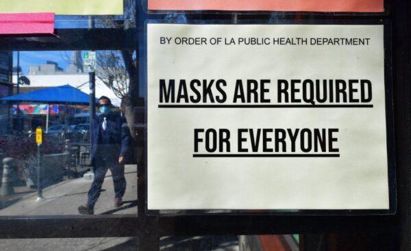 A man wearing a face mask walks past a sign stating a mask requirement posted on a storefront in Los Angeles on March 2, 2022. (Frederic J. Brown/AFP via Getty Images)