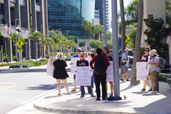 Protesters hold signs criticizing Fla. Gov. Ron DeSantis while he was making a speech nearby in downtown Tampa on July 15, 2022. (Natasha Holt/The Epoch Times)