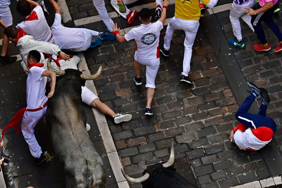Runners fall as people run in the street with fighting bulls during the running of the bulls at the San Fermin Festival in Pamplona, northern Spain, on July 9, 2022. (Alvaro Barrientos/AP Photo)