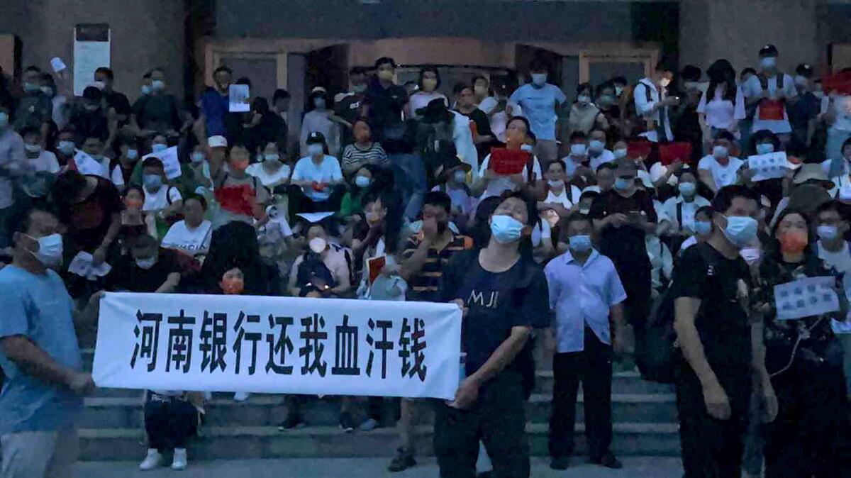 People hold banners and chant slogans to stage a protest at the entrance to a branch of China's central bank in Zhengzhou, in central China's Henan Province, on July 10, 2022. A large crowd of angry Chinese bank depositors faced off with police, some reportedly injured as they were roughly taken away, in a case that has drawn attention because of earlier attempts to use a COVID-19 tracking app to prevent them from mobilizing. (Yang/AP Photo)