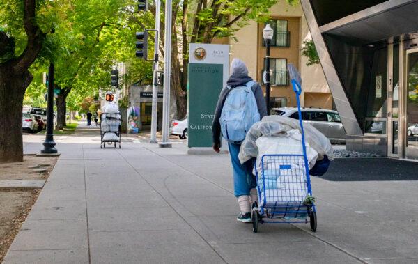 A homeless person pulls a cart of items on a sidewalk in Sacramento, Calif., on April 18, 2022. (John Fredricks/The Epoch Times)