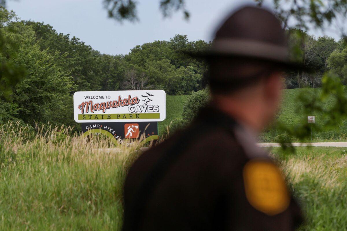 An Iowa State Patrolman walks past a Maquoketa Caves State Park sign as police investigate a shooting that left several people dead, in Maquoketa, Iowa, on July 22, 2022. (Nikos Frazier/Quad City Times via AP)
