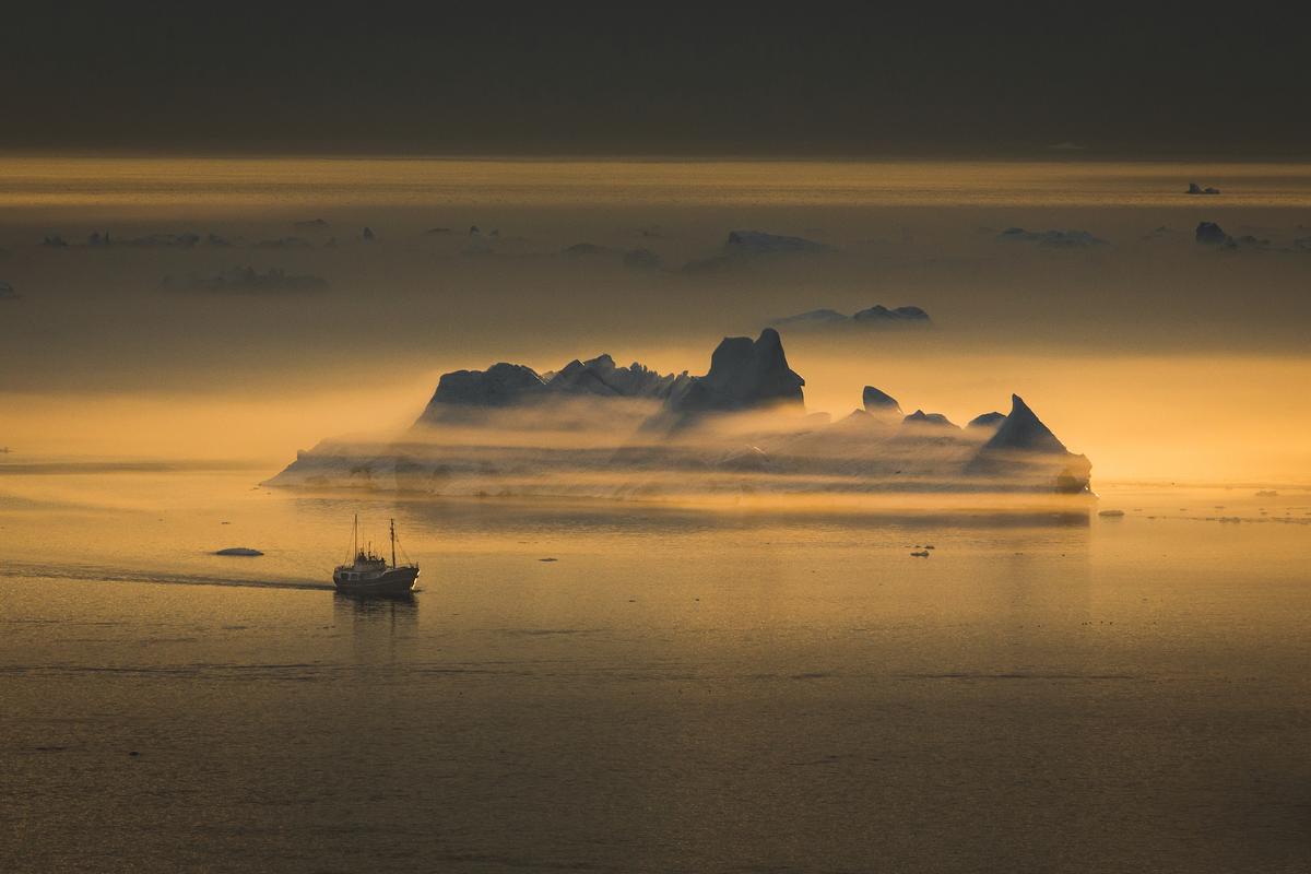 A fishing vessel passes an iceberg shrouded in fog near Ilulissat. (Visit Greenland)
