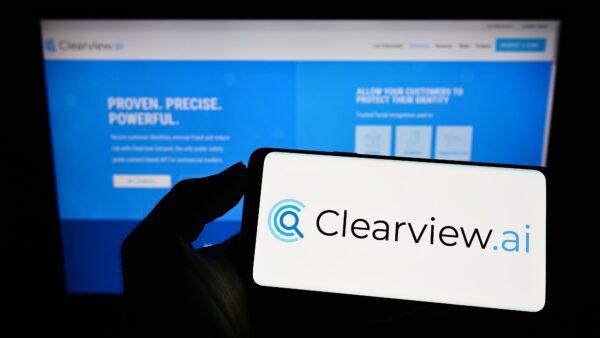 A cellphone is held with the logo of facial recognition company Clearview AI Inc. on the screen in front of the business webpage. (T. Schneider/Shutterstock)
