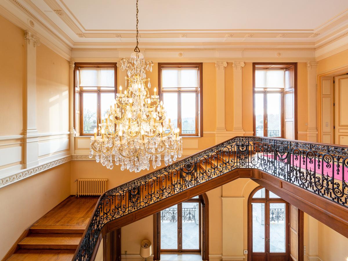 Large windows and a magnificent crystal chandelier light up the grand staircase leading to the residences. (Courtesy of Belgium Sotheby’s International Realty)