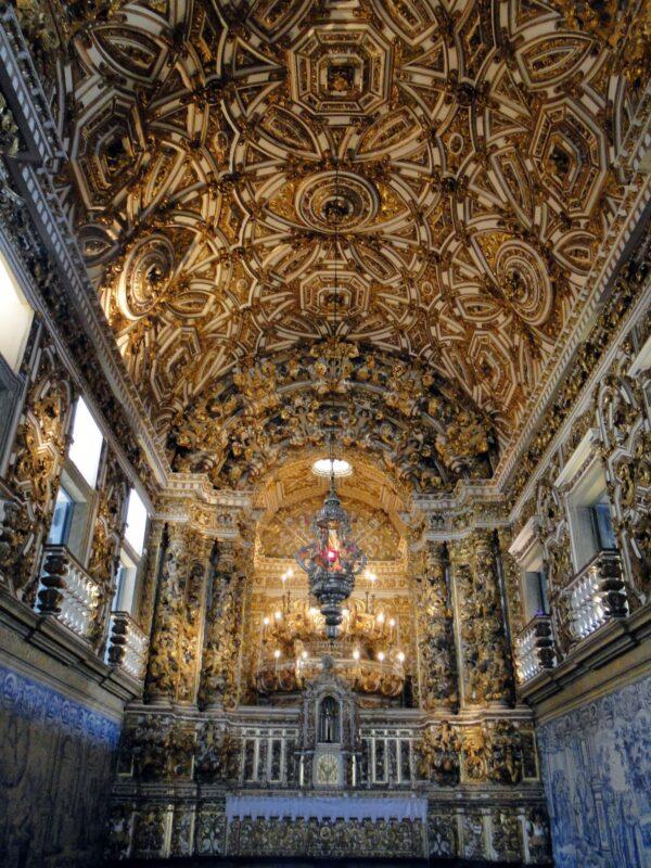 When visitors enter the church, they are greeted by a lavishly decorated interior. The impressive detailing enhances its architectural beauty through panels of azulejos, sacred paintings, and extensive use of gilding. The ceiling has impressive sculpted woodwork with gilded finishes and a hanging lamp. Golden foliage continues throughout the interior, on the sculpted columns and arches, and on the eight columns supporting the side altars. About one ton of gold was used in the church and convent, which were built with local sandstone from Bahia, a state in Brazil.  (<a href="https://commons.wikimedia.org/wiki/File:Leon_Petrosyan,_Reinhard_Selten_with_his_wife_(Saint_Petersburg_State_University).JPG">Leon Petrosyan</a>/ <a href="https://creativecommons.org/licenses/by-sa/4.0/deed.en">CC BY-SA 4.0</a>)