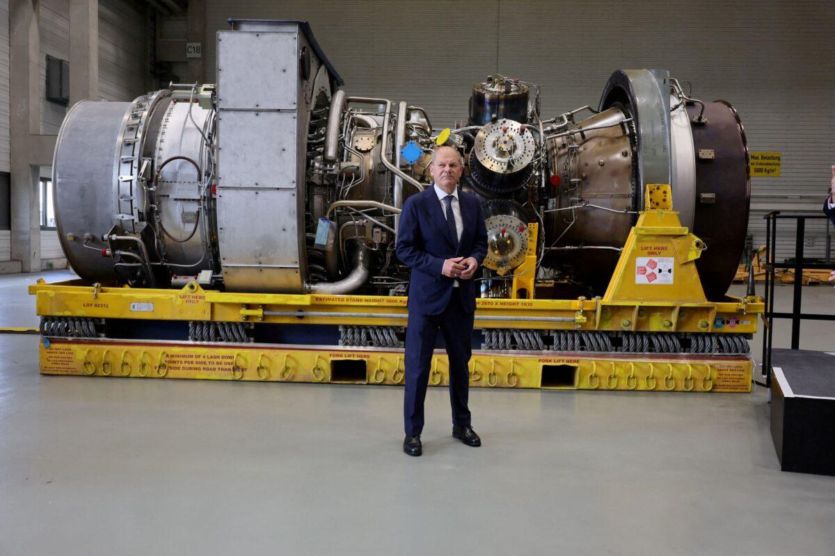 German Chancellor Olaf Scholz stands next to a gas turbine meant to be transported to the compressor station of the Nord Stream 1 gas pipeline in Russia during his visit to Siemens Energy's site in Muelheim an der Ruhr, Germany, on Aug. 3, 2022. (Wolfgang Rattay/Reuters)