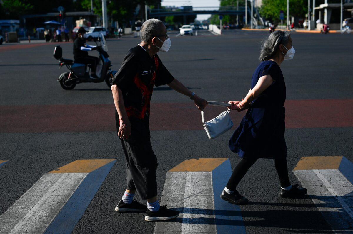 A woman leads an elderly man across a street in Beijing on June 2, 2022. (Wang Zhao/AFP via Getty Images)