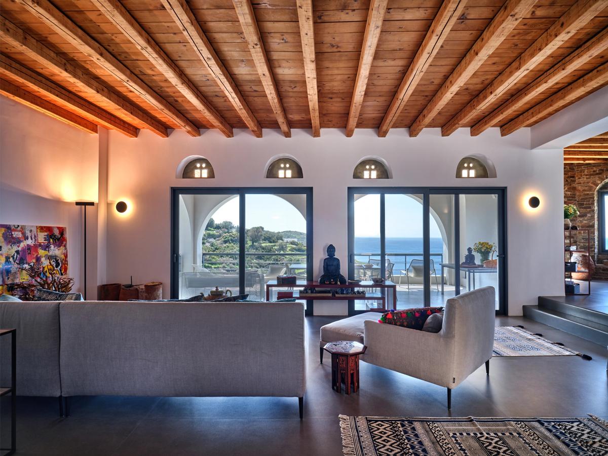  The modern Cycladic architecture is a Spartan mix of stylish accents and simplistic livability. Here, you have one of the living spaces, with wood beams and large glass areas for capturing the spellbinding views of the Aegean. (Courtesy of Greece Sotheby's International Realty)