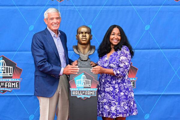 Melanie Mills, widow of former NFL player Sam Mills, right, and Jim Mora pose with his bust during an induction ceremony at the Pro Football Hall of Fame in Canton, Ohio, Saturday, Aug. 6, 2022. (David Dermer/AP Photo)