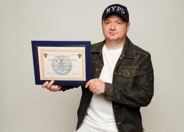 Unvaccinated and terminated NYPD police officer Marjel Kola, with his "Cop of the Month" certificate of service achievement on Aug. 8, 2022. (Dave Paone/The Epoch Times)
