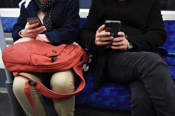 A close-up of an unidentifiable man and woman sitting next to each other on the Tube, both looking at their phones. (Kirsty O’Connor/PA Media)