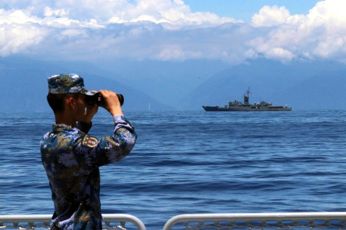A People's Liberation Army member looks through binoculars during military exercises as Taiwan's frigate Lan Yang is seen in the background on Aug. 5, 2022. (Lin Jian/Xinhua via AP, File)