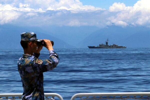 A member of China's People's Liberation Army looks through binoculars during military exercises as Taiwan's frigate Lan Yang is seen in the background on Aug. 5, 2022. (Lin Jian/Xinhua via AP)