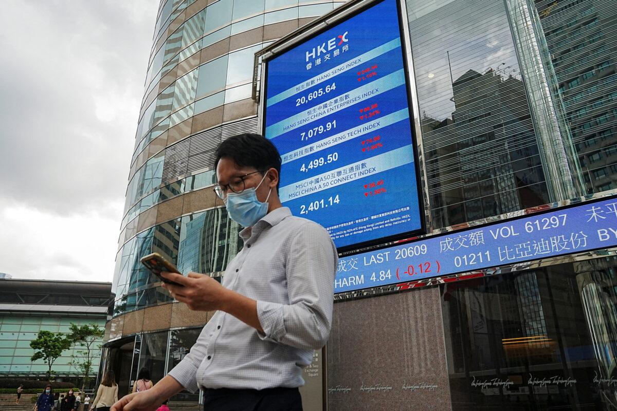 People walk past a screen displaying the Hang Seng stock index outside Hong Kong Exchanges, in Hong Kong, on July 19, 2022. (Lam Yik/Reuters)