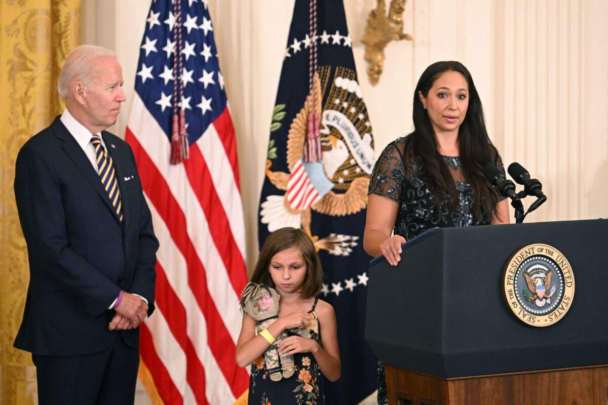 Brielle Robinson, daughter of Sgt. First Class Heath Robinson, listens as her mother, Danielle Robinson, speaks during a signing ceremony for the "Sergeant First Class Heath Robinson Honoring our Promises to Address Comprehensive Toxics (PACT) Act of 2022," in the East Room of the White House, on Aug. 10, 2022. The legislation allowed for delivery of more timely benefits and services to veterans who may have been impacted by toxic exposures while serving in the U.S. armed forces. Sgt. First Class Heath Robinson died from lung cancer as a result of toxic exposure. [Author's Note: military families with a spouse deploying during the global war on terror will recognize Brielle holds a "daddy doll"—a doll with the picture of her father affixed to it.] (Jim Watson/AFP via Getty Images)