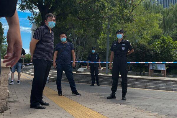 Plainclothes policemen and security guards wearing face masks stand guard as they stop journalists preventing them from getting near the No. 1 Intermediate People's Court in Beijing on Aug. 10, 2022. (Andy Wong/AP Photo)