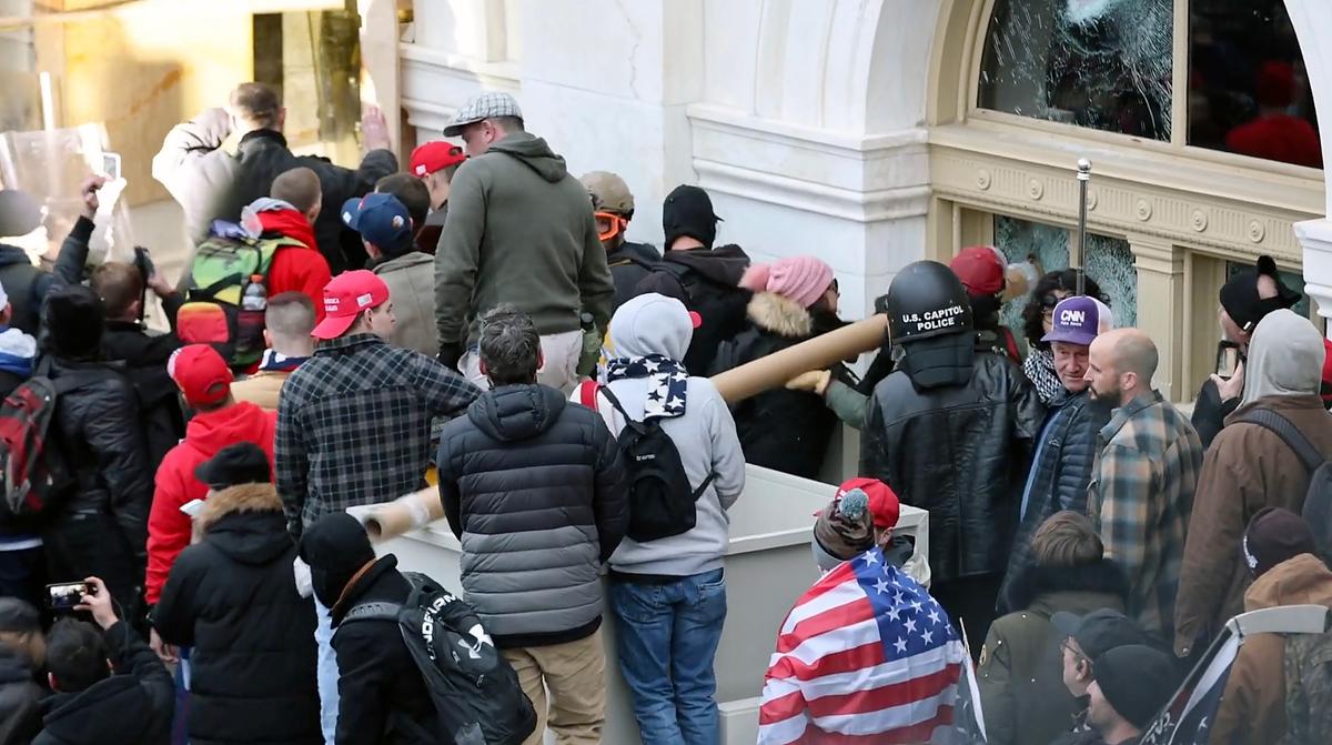 Rioters use a heavy-duty cardboard tube to smash in a window adjacent to the Lower West Terrace tunnel at the U.S. Capitol on Jan. 6, 2021. (Christopher Chern via Storyful)