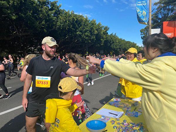 Falun Gong practitioners in Sydney demonstrate Falun Gong exercises on the Rose Bay section of the annual charity run City2Surf on Aug. 14, 2022. The picture shows a runner receiving a lotus flower from a Falun Gong practitioner. (The Epoch Times)