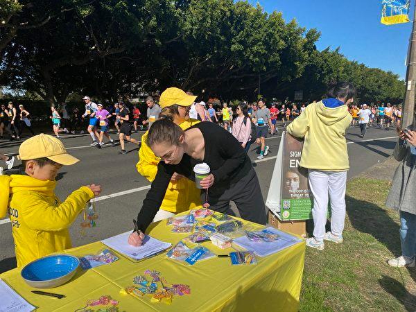 Sydney Falun Gong practitioner demonstrated exercises and collected signatures at the finish line. Vanessa Arbon signed to support the“End CCP” campaign. (The Epoch Times)