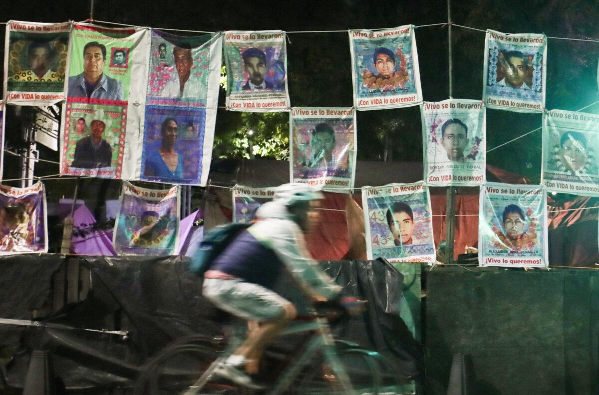 A person cycles past a wall with pictures of some of the 43 students who disappeared in 2014 from the Ayotzinapa Rural Teachers' College, in Mexico City, on Aug. 19, 2022. (Henry Romero/Reuters)