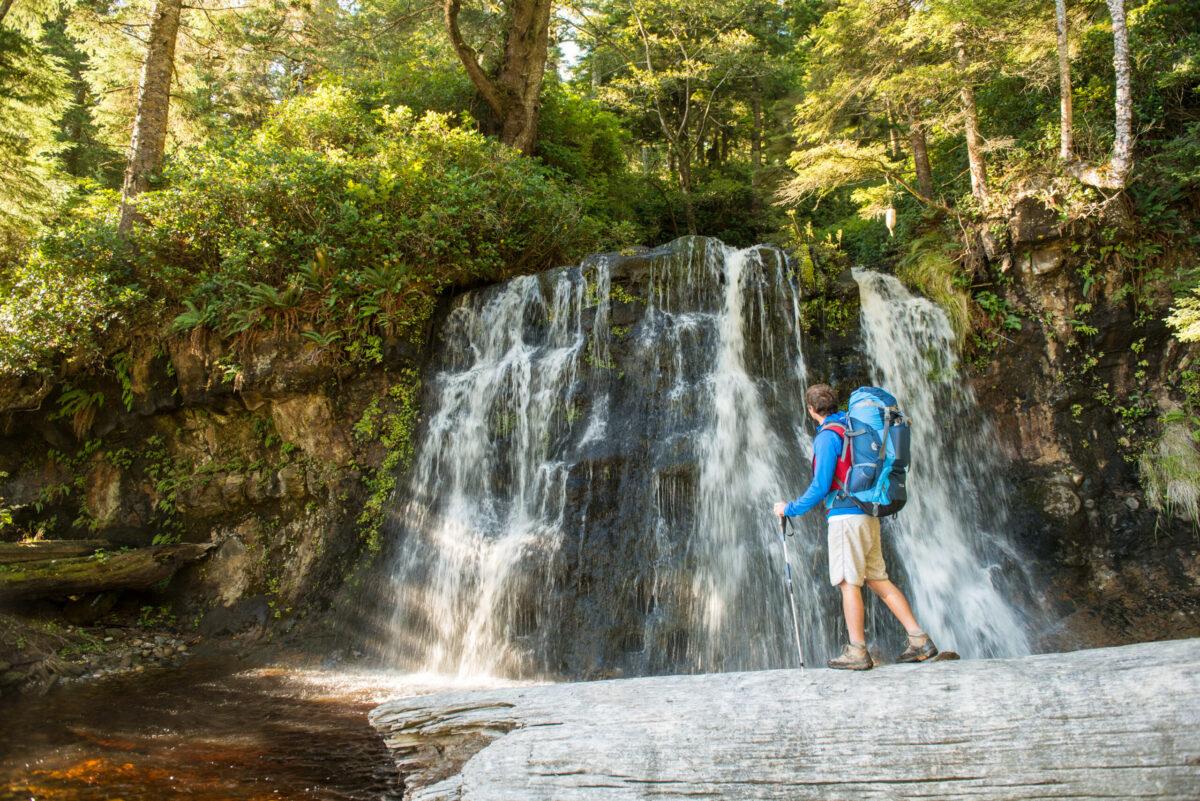 A hiker marvels at the picturesque waterfall at Bonilla Creek, on the West Coast Trail. Pacific Rim National Park Reserve. (Parks Canada / Scott Munn.)