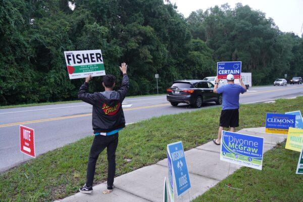 Volunteers for opposing school board candidates in a heated race in Alachua County wave to passing cars outside a Gainesville, Fla. voting site on Aug. 23. (Nanette Holt/The Epoch Times)