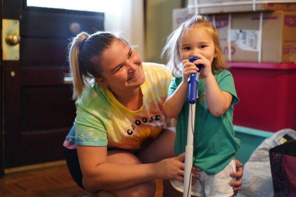 Briana Austin looks on as her daughter Autumn plays with her new toy microphone at Vivian Van Orden's house in Port Jervis on Aug. 22, 2022. (Cara Ding/The Epoch Times)