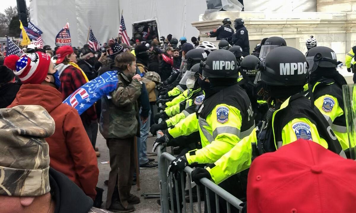 Mark Griffin, wearing a Trump flag as a cape, chats with police just before being shot in the leg at the U.S. Capitol on Jan. 6, 2021. (Steve Baker/Screenshot via The Epoch Times)