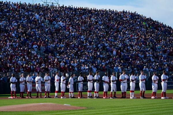 Cincinnati Reds players stand with fans for the national anthem before a baseball game against the Chicago Cubs at the Field of Dreams movie site in Dyersville, Iowa, Aug. 11, 2022. (Charlie Neibergall/AP Photo)