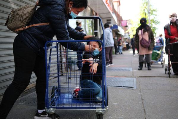 A woman fixes her child's mask as hundreds of people wait in line for food outside of a Brooklyn mosque and cultural centre in New York City, on May 22, 2020. (Spencer Platt/Getty Images)