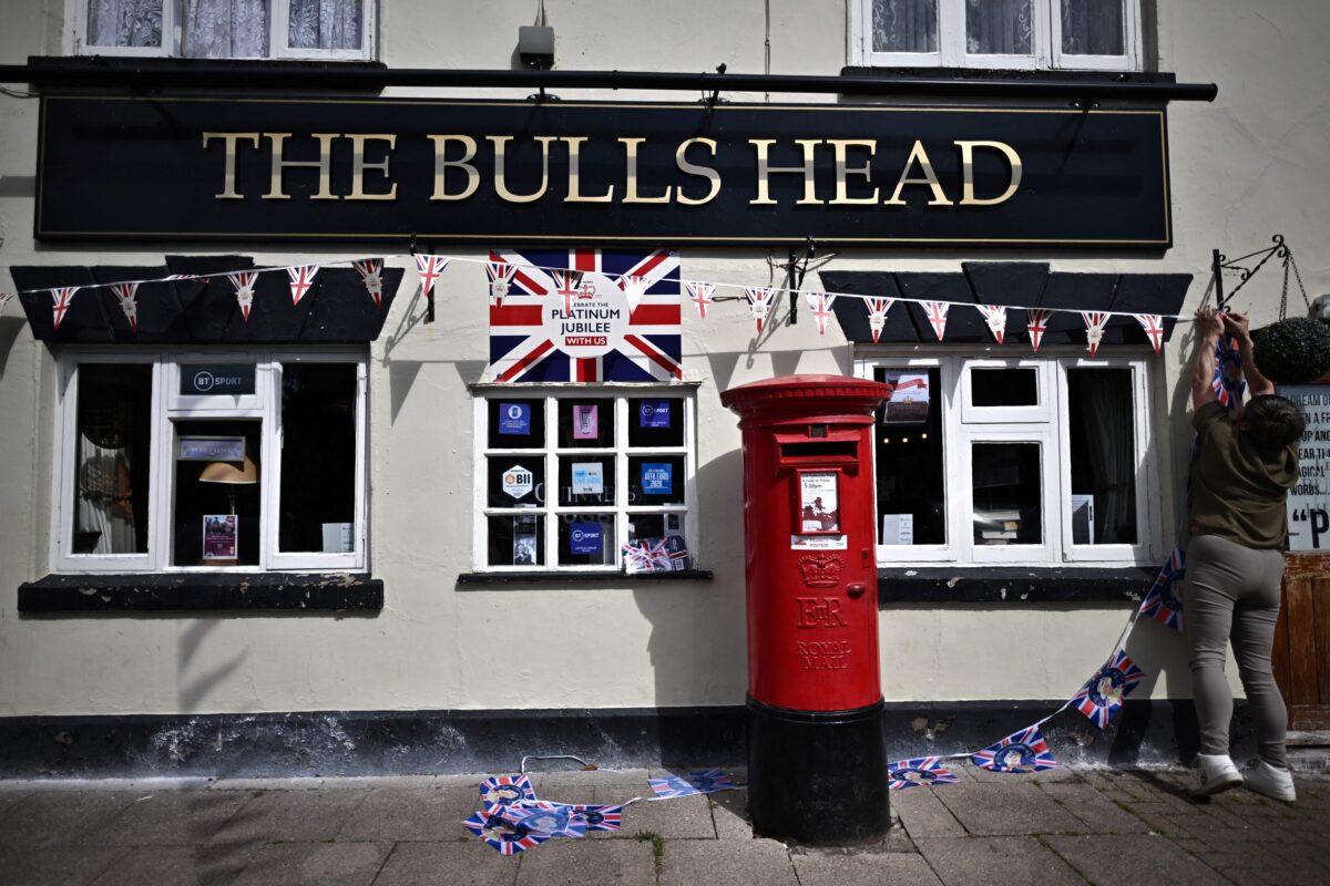 A member of staff of the Bulls heads pub hangs a bunting on the facade of the bar, as preparations get underway for the forthcoming Platinum Jubilee celebrations for Queen Elizabeth II, in Bidford-On-Avon, central England, on May 27, 2022. (Ben Stansall/AFP via Getty Images)