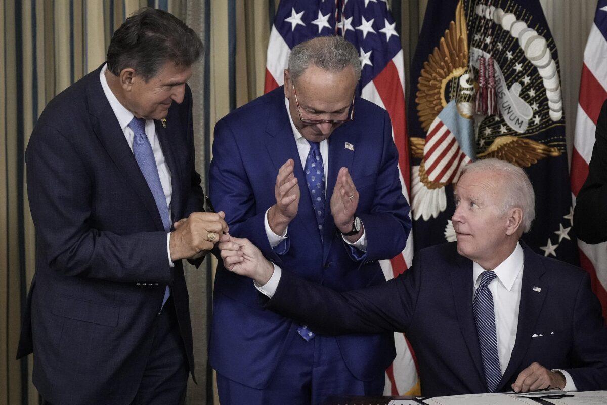 With Senate Majority Leader Charles Schumer (D-N.Y.) looking on, President Joe Biden hands Sen. Joe Manchin (D-W.Va.) the pen he used to sign into law the Inflation Reduction Act at the White House in Washington, on Aug. 16. (Drew Angerer/Getty Images)