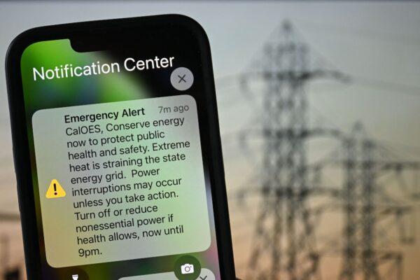 A photo illustration shows a background of electric power infrastructure with an Apple iPhone showing an Emergency Alert notification from CalOES urging the public to conserve energy to protect health and safety as the electricity grid is strained during a heat wave in Los Angeles, Calif., on Sept. 6, 2022. (Patrick T. Fallon/AFP via Getty Images)